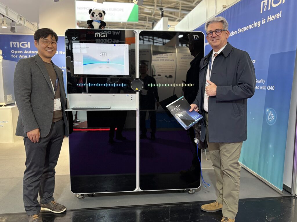 Miguel Oliveira standing beside MGI’s T7+ sequencing platform with an MGI representative at analytica 2026 in Munich.